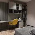 Modern çalışma alanı tasarımı; gri tonlarda modüler duvar ünitesi, sarı ofis sandalyesi ve minimalist dekor.