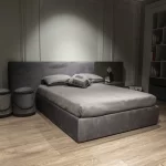 Modern genç odası tasarımı; düz başlıklı gri yatak, minimal komodin ve açık raf detaylarıyla sade dekorasyon.